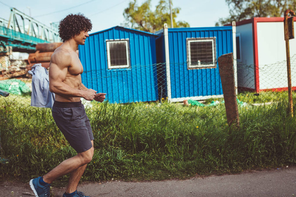 fitter muskulöser junger männlicher Läufer mit nacktem Oberkörper sprintet auf Brückenstufen - Foto, Bild