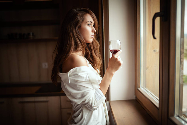 νεαρή ρομαντική γυναίκα πίνοντας κόκκινο κρασί στην κουζίνα - Φωτογραφία, εικόνα