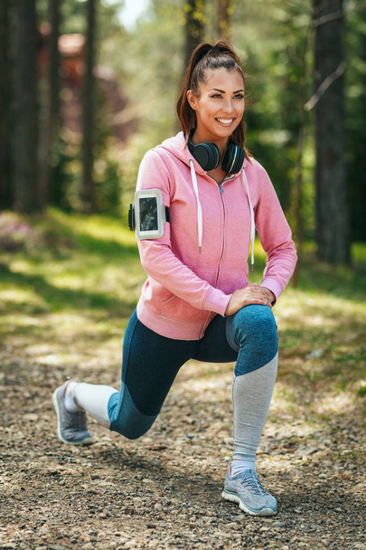 Happy woman in pastel sportswear listening to music and stretching in sunny forest - 写真・画像