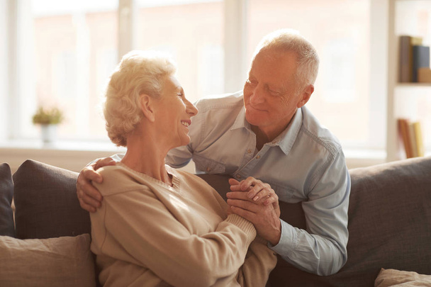 Porträt eines liebenden Senioren-Paares, das sich gegenseitig ansieht, während es zu Hause im Sonnenlicht posiert, Kopierraum - Foto, Bild