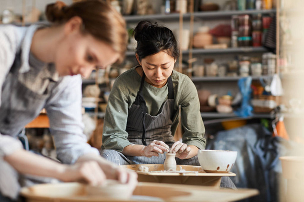 Серйозний кваліфікованих молодих азіатських жіночий Поттер в фартух сидить на гончарному колі і виготовлення глиняної вази з рук в майстерні - Фото, зображення