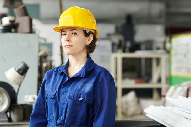 Retrato de una trabajadora confiada que lleva casco mirando a la cámara mientras posa en la fábrica, espacio para copiar
 - Foto, Imagen