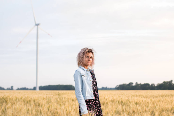 young tanned curly haired woman in denim jacket and dress on the field of ripened wheat, sunset time - Foto, imagen