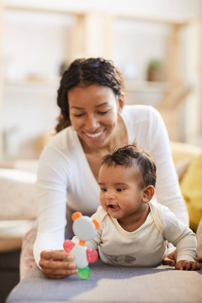 Jovem mãe negra feliz mostrando brinquedo bonito para dentição para menino animado no sofá, bebê explorando conceito de mundo
 - Foto, Imagem
