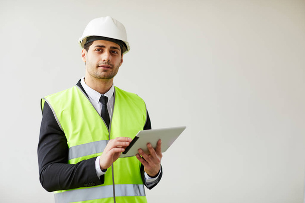 Waist up portrait of  Middle-Eastern engineer wearing hardhat posing against white background  holding tablet, copy space - Foto, immagini