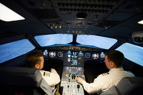 航空機のコントロールパネルに座って飛行の準備をするストライプと白いシャツで深刻な集中パイロットの背面図 - 写真・画像