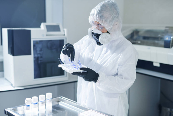 Elfoglalt fertőző betegség tudós Biohazard öltöny és a légzőmaszk áll az asztalnál az üvegek, és figyelembe minták bioveszélyek a kutatás - Fotó, kép