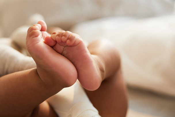 Close-up de irreconhecível bonito bebê tremendo pés enquanto deitado na cama, conceito de inocência
 - Foto, Imagem
