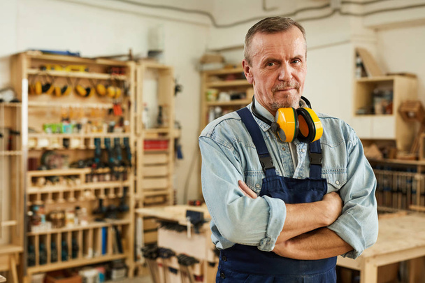 Waist up portrait of confident senior carpenter looking at camera while posing in joinery, copy space - Photo, Image