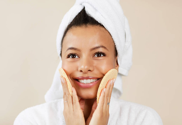 Cabeça e ombros retrato de mulher de raça mista sorrindo massageando seu rosto com esponjas durante a rotina de cuidados com a pele da manhã, espaço de cópia
 - Foto, Imagem