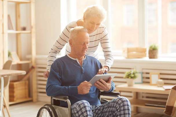 Portrét staršího muže v invalidním vozíku, který používá digitální tablet osvětlený slunečním zářením, místo kopírování - Fotografie, Obrázek