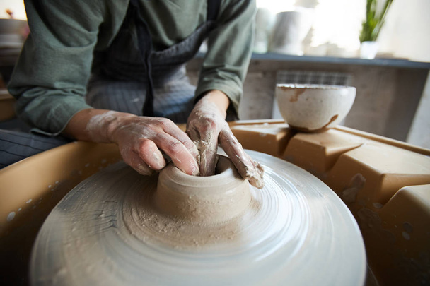 Nahaufnahme einer unkenntlichen Frau mit schmutzigen Händen, die ein Loch in Ton macht, während sie Vase auf Töpferscheibe modelliert - Foto, Bild
