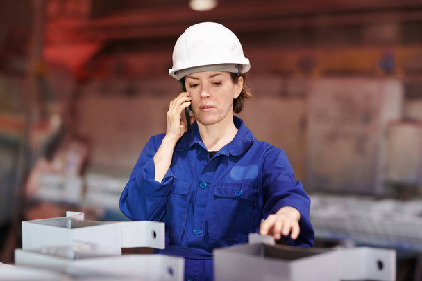 Vyötärö ylös muotokuva naispuolinen työntekijä puhuu puhelimitse valvoessaan tuotantoa tehtaalla, kopioi tilaa
 - Valokuva, kuva
