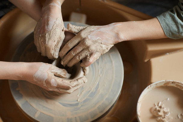 Hochwinkelaufnahme von nicht wiedererkennbaren Frauen mit Händen, die mit Ton beschmiert sind, indem sie Töpferscheibe benutzen, während sie Vase formen - Foto, Bild