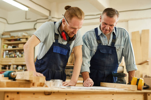 Waist up  portrait of senior carpenter teaching apprentice  while working together  in joinery workshop - Photo, Image