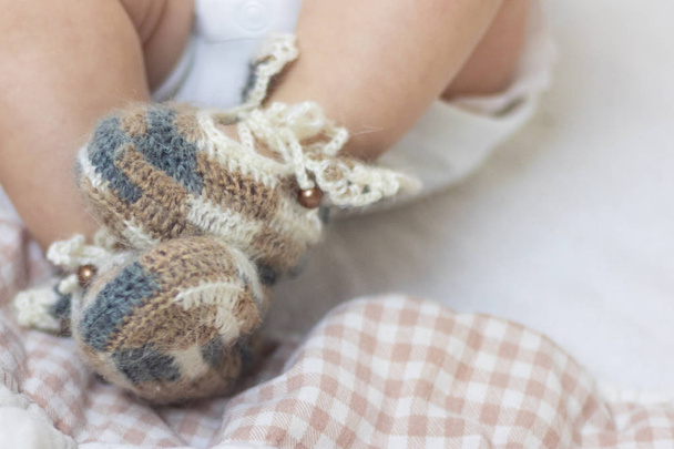 Newborn baby feet close up in wool brown knitted socks booties on a white blanket. The baby is in the crib. - Foto, Imagem