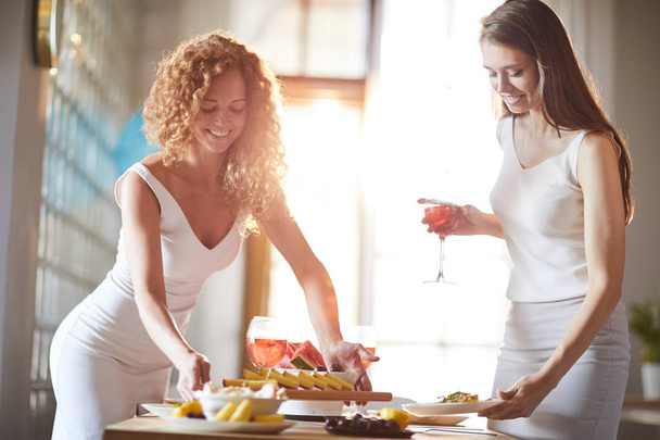 Πορτραίτο δύο όμορφων νεαρών γυναικών που τακτοποιώντας φαγητό στο τραπέζι για δείπνο στο φως του ήλιου, αντιγραφή χώρου - Φωτογραφία, εικόνα