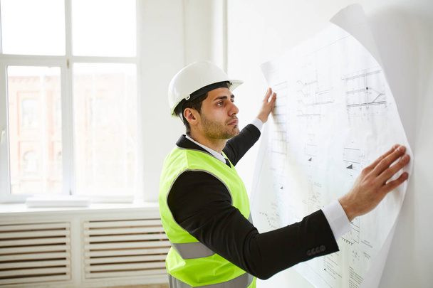 Side view portrait of  Middle-Eastern engineer  holding plans against wall  while standing on construction site, copy space - Photo, Image
