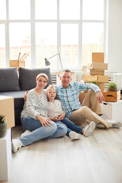 Portrét pozitivní sjednocené rodiny v příležitostných oblecích, sedících na parketové podlaze a v obývacím pokoji s lepenkovou krabicí. - Fotografie, Obrázek