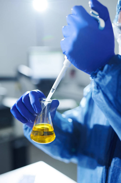Gros plan d'un travailleur de laboratoire méconnaissable dans des gants stériles qui dépose un réactif dans une fiole avec de l'urine pendant ses recherches
 - Photo, image
