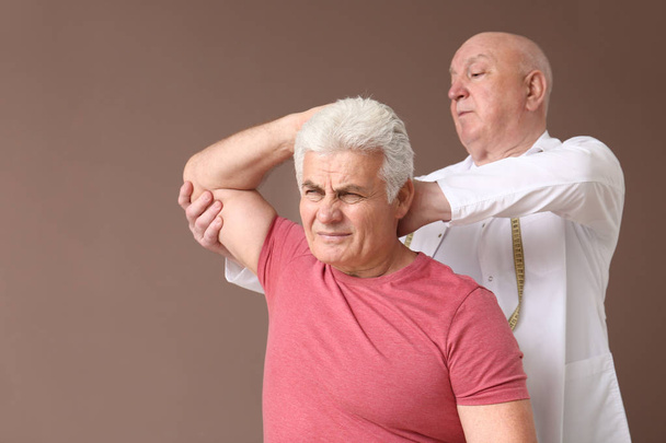 Senior physiotherapist working with mature man on color background - Fotó, kép