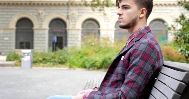 Confident young man look sitting on bench and smiling - Кадри, відео