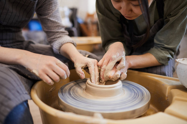 Primo piano di abile ceramista asiatica che mostra alla donna come modellare il piatto di argilla usando la ruota in ceramica in officina
 - Foto, immagini