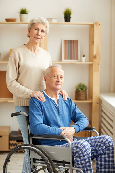 Portrét starší ženy, která se objímá manžela sedícího v invalidním křesle, jak se dívá na kameru, místo kopírování - Fotografie, Obrázek
