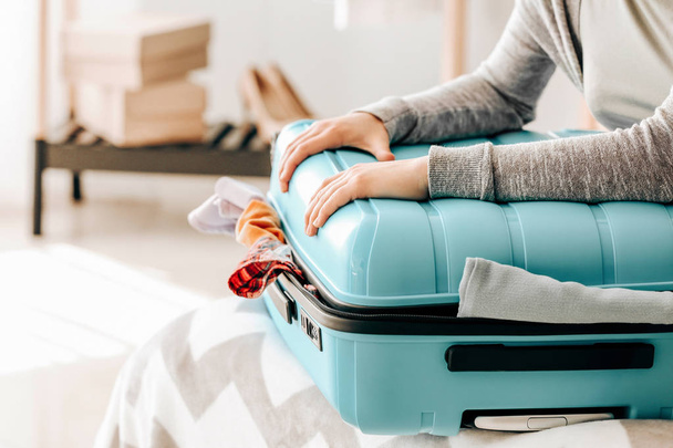 Женщина пытается закрыть чемодан кучей вещей. Концепция путешествия
 - Фото, изображение