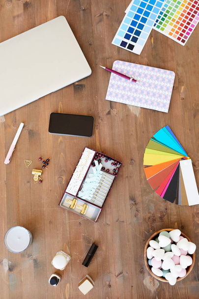 Overview of color swatches and palette, notebook with pen, smartphone, laptop, self-love items and bowl of marshmallows on wooden table - Foto, Bild