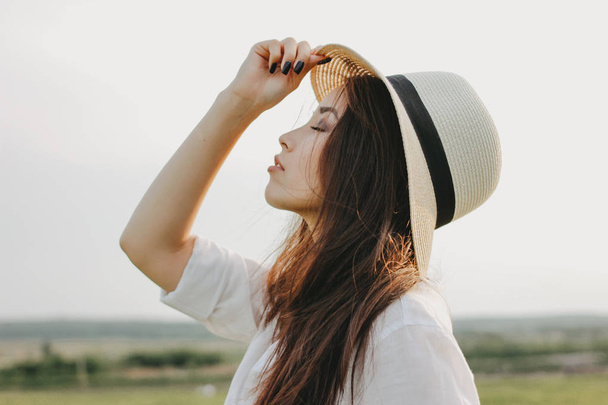Портрет чарівного безтурботного довгого волосся азіатської дівчини в білому одязі і солом'яному капелюсі насолоджується життям у полі на заході сонця. Чутливість до концепції природи
 - Фото, зображення