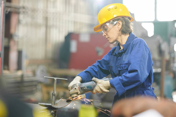 Endüstriyel fabrikada veya garajda metal kesen olgun kadın işçinin yan görünüm portresi, kopyalama alanı - Fotoğraf, Görsel