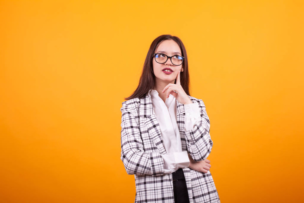 Cute caucasian girl with eyeglasses looking up and thoughtful over yellow background - Foto, Imagem