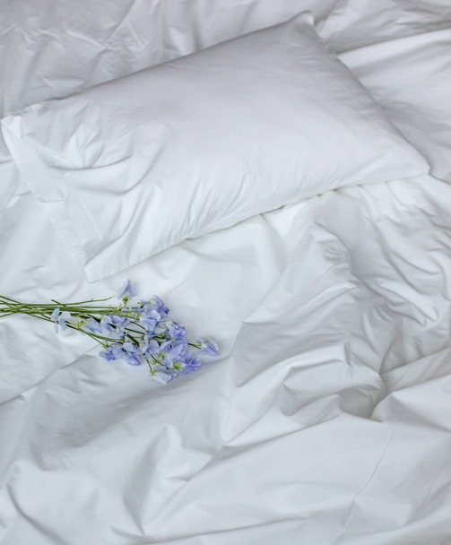 Flowers on the messy bed, white bedding items and blue flowers bouqet - Photo, Image