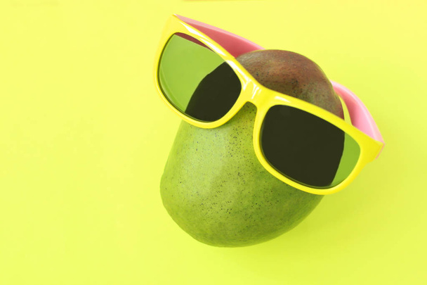 Dojrzałe soczyste zielone i czerwone Mango w okulary przeciwsłoneczne na pastelowych żółtym tle. Kopiuj przestrzeń. minimalistyczny styl. - Zdjęcie, obraz