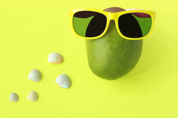 Zralý šťavnatý zelený a červený mango v slunečních brýlích na pastelově žlutém pozadí. Kopírovat místo minimalistický styl. - Fotografie, Obrázek