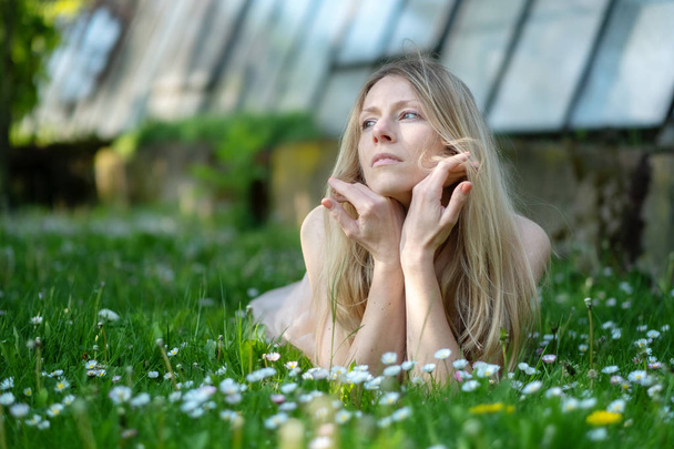 Mujer rubia acostada pensativamente en un campo Jardín con margaritas
 - Foto, imagen