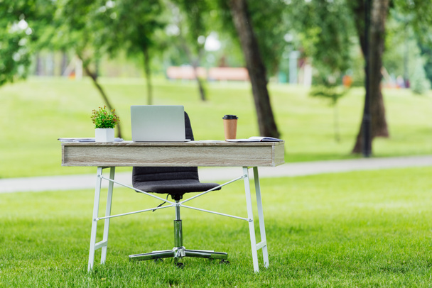 selective focus of office table with different office stuff near office chair in park - Foto, Imagen