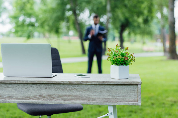 selective focus of table with flowerpot and laptop in park  - Photo, Image