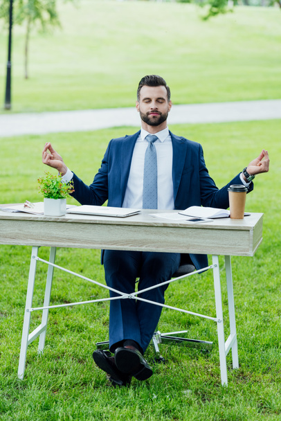 elölről véve a csinos, fiatal üzletember formális kopás meditál ülve asztalnál különböző irodai cucc a parkban  - Fotó, kép