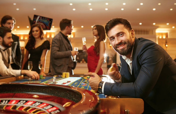 Un homme en costume avec un verre de whisky assis à la table de roulette jouant au poker dans un casino
. - Photo, image