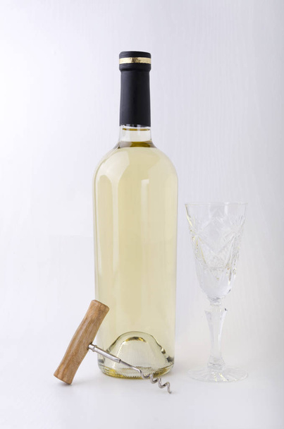 Παλιομοδίτικο ποτήρι κρασιού, σφραγισμένο μπουκάλι κρασί και ανοιχτήρι στη λευκή επιφάνεια από λευκό τοίχο - Φωτογραφία, εικόνα