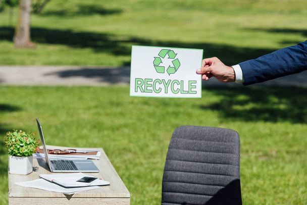 wykadrowany widok biznesmen legitymacji z recyklingu znak w pobliżu tabeli w parku - Zdjęcie, obraz