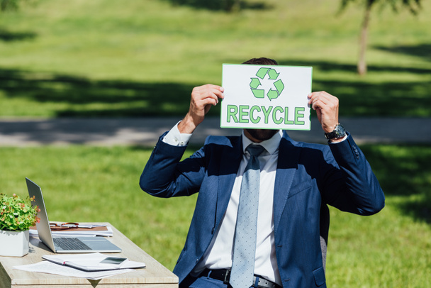 young businessman sitting near table and covering face with card with recycle lettering - Foto, immagini