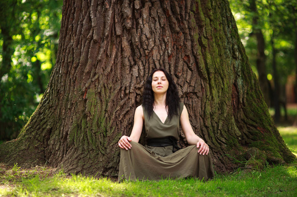 Girl in dress sits enjoying nature meditates, practices yoga - Foto, immagini