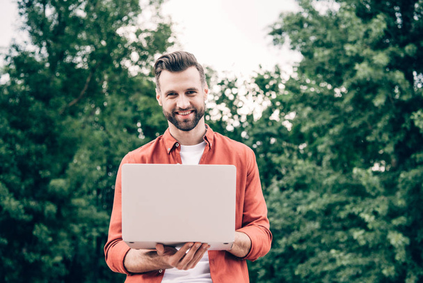 young man standing in park, holding laptop and looking at camera - Foto, Bild