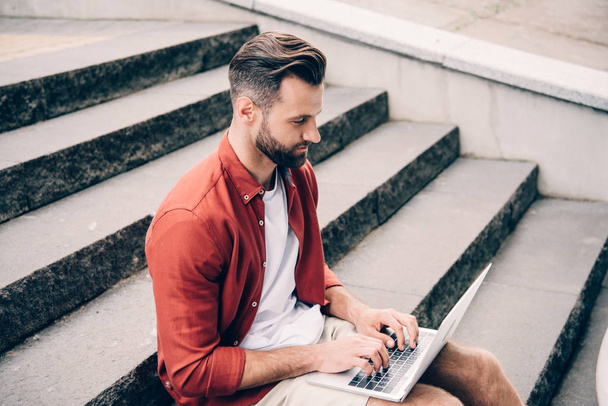 young man using laptop while sitting on stone stairs - Valokuva, kuva