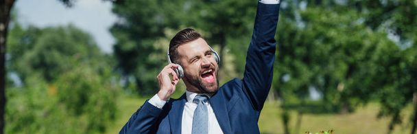 tiro panorâmico de excitado jovem empresário ouvindo música e subindo a mão no ar
 - Foto, Imagem