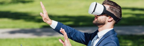 panoramic shot of businessman gesturing in VR headset  - Фото, изображение