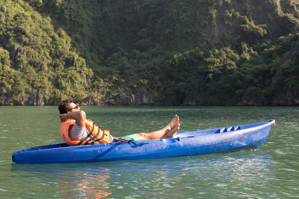 Viajante caucasiano relaxante em um caiaque azul águas serenas
 - Foto, Imagem